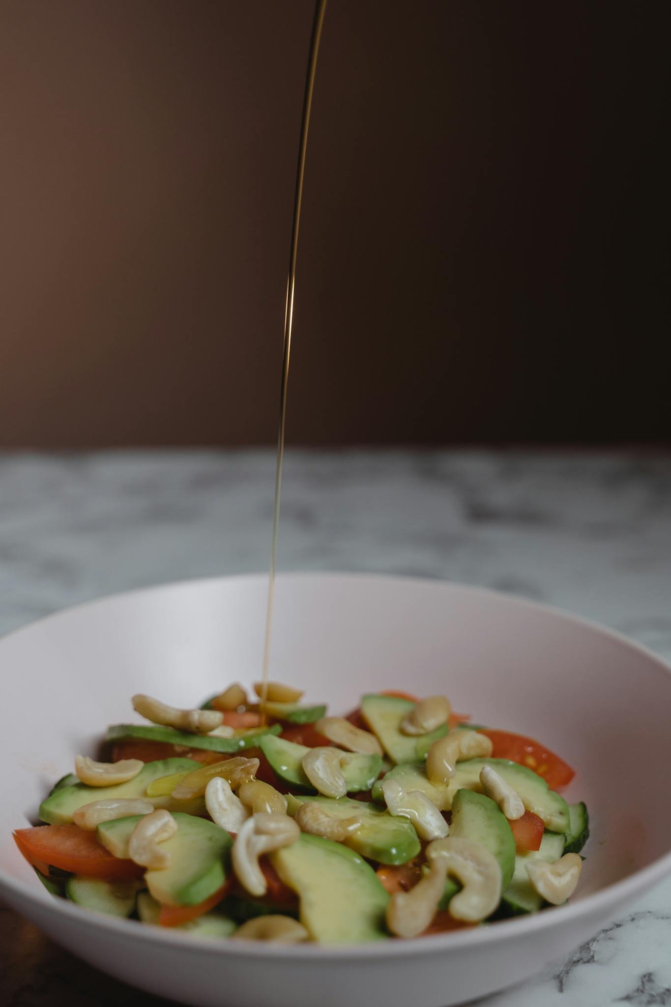 Vibrant salad with cucumbers, tomatoes, and cashews drizzled with dressing.