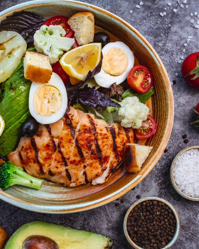 Top view of keto-friendly grilled chicken salad with fresh avocado, tomato, broccoli, and cauliflower
